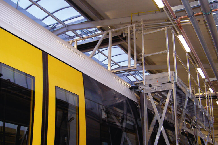 In einer Werkshalle steht eine Arbeitsbühne an einer gelb-weißen Straßenbahn in Arbeitshöhe des Fahrzeugdaches.