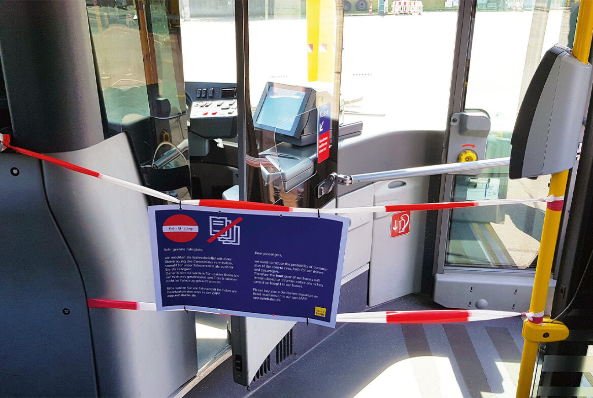 Ein stehender Linienbus mit geöffneter Eingangstür vom Gang aus abgebildet. Der ganze Bereich ist mit rot-weißem Absperrband gesichert und mit einer blauen Informationstafel ausgestattet.