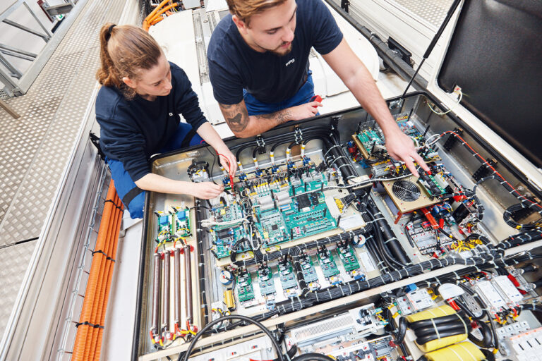Ein junger Mann und eine junge Frau arbeiten an einem elektronischen Schaltkasten.