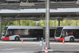 zwei moderne elektrische Linienbusse in weiß mit roten Akzenten in einem überdachten Bus-Port